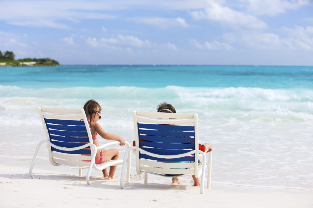 Kinder sitzen in Stühlen am karibischen Strand und blicken aufs Meer