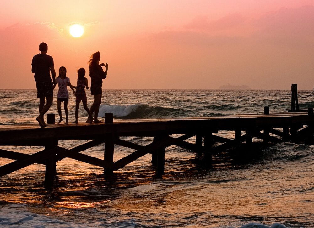 Familie auf Steg am Strand im Sonnenuntergang.